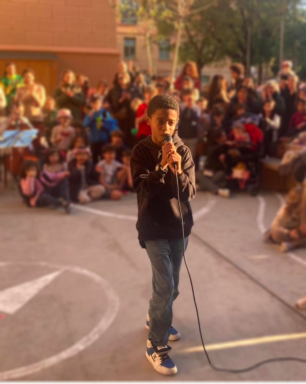 Un nen cantant amb micròfon davant del públic de l'escola